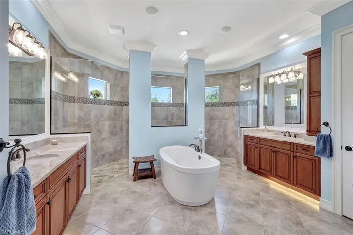 Bathroom featuring a walk in shower, two vanities, a sink, a soaking tub, and crown molding