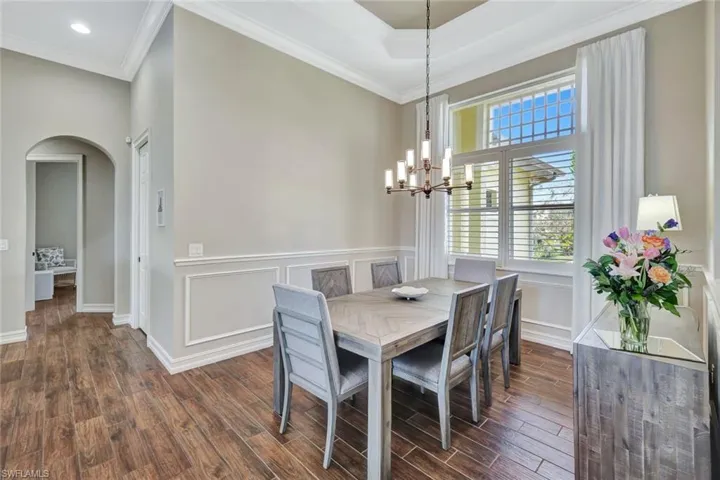 Dining area featuring arched walkways, dark wood finished floors, ornamental molding, an inviting chandelier, and a decorative wall