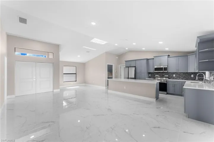 Kitchen with decorative backsplash, a center island, appliances with stainless steel finishes, light tile patterned floors, and gray cabinetry