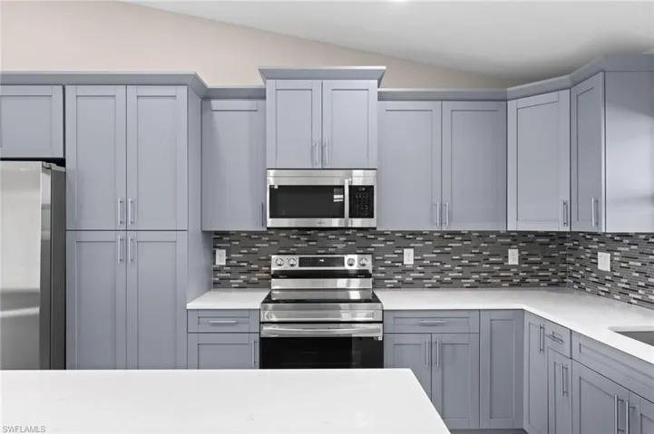 Kitchen featuring lofted ceiling, tasteful backsplash, appliances with stainless steel finishes, and gray cabinetry