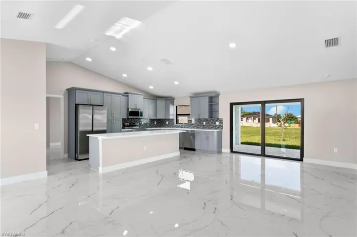 Kitchen featuring light tile patterned floors, a kitchen island, stainless steel appliances, decorative backsplash, and vaulted ceiling