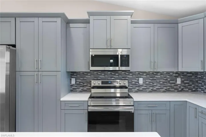 Kitchen featuring decorative backsplash, appliances with stainless steel finishes, gray cabinets, and vaulted ceiling