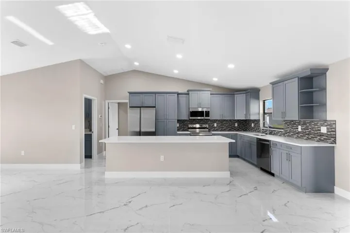 Kitchen with tasteful backsplash, stainless steel appliances, gray cabinetry, vaulted ceiling, and a center island