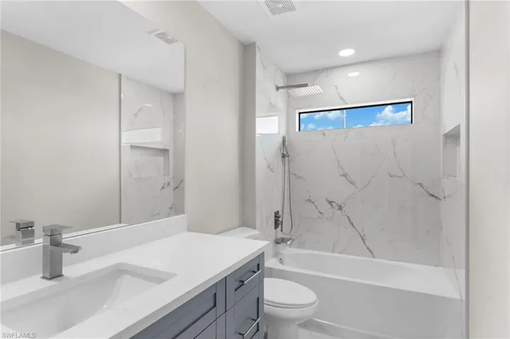 Full bathroom featuring vanity, tiled shower / bath combo, and toilet