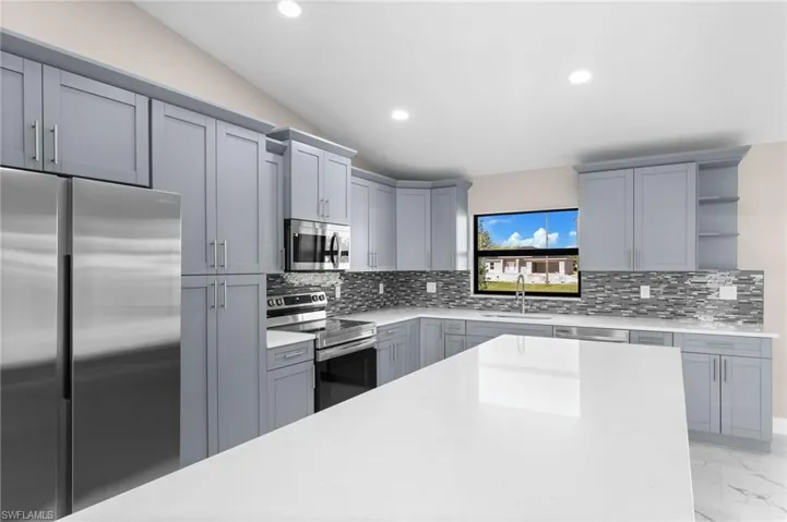 Kitchen with light tile patterned flooring, backsplash, gray cabinets, stainless steel appliances, and sink