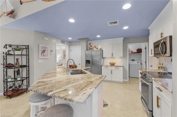 Kitchen featuring appliances with stainless steel finishes, a kitchen island with sink, tasteful backsplash, washer / clothes dryer, and a breakfast bar