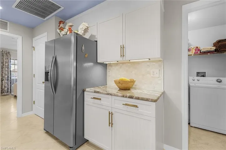 Kitchen with washer / clothes dryer, light stone counters, decorative backsplash, light tile patterned floors, and white cabinetry