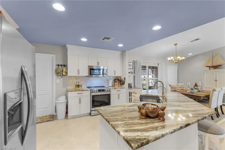 Kitchen with appliances with stainless steel finishes, a large island, white cabinets, hanging light fixtures, and recessed lighting