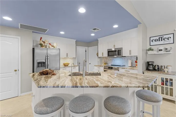 Kitchen with white cabinets, stainless steel appliances, light stone countertops, a kitchen bar, and a kitchen island with sink