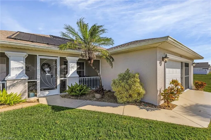 Ranch-style home featuring stucco siding, an attached garage, a front yard, and solar panels
