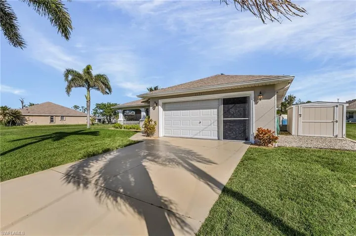Single story home featuring a front lawn, stucco siding, driveway, a garage, and a storage unit