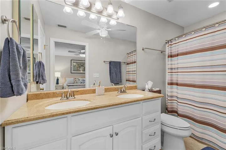 Ensuite bathroom with double vanity, a shower with shower curtain, a ceiling fan, and light tile patterned floors