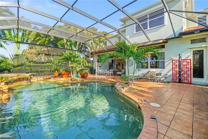 Screened swimming pool enclosure featuring a waterfall rock feature, stamped concrete patio, and tropical landscaping