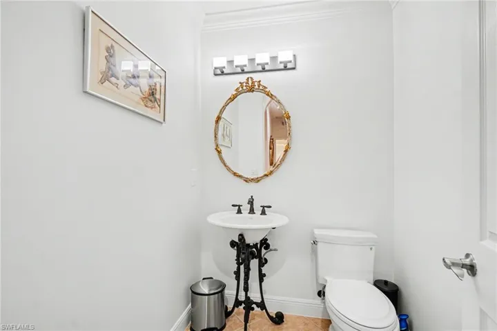 Bathroom featuring a pedestal sink with an ornate black metal base, a circular gold-framed mirror, a vanity light fixture, and crown molding