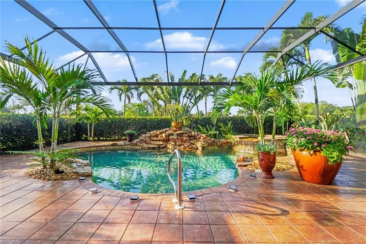 Screened-in pool area featuring a freeform swimming pool with rock waterfall, integrated palm trees, and stamped concrete decking