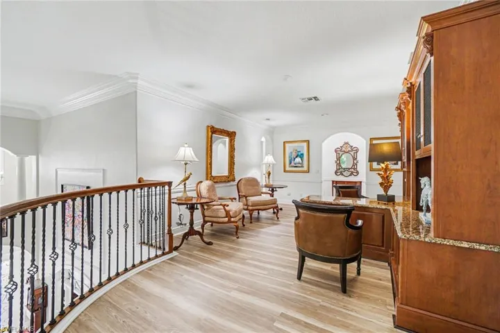 Upper landing featuring light wood-finish flooring, an ornate wrought iron and wood banister, extensive crown molding, and an arched entryway
