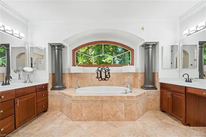 Soaking tub with tile surround, flanked by decorative columns and an arched window