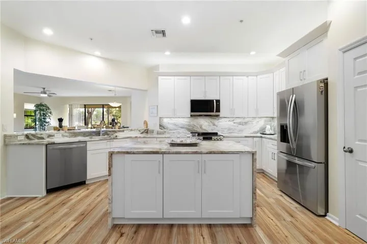 Kitchen with appliances with stainless steel finishes, white cabinetry, a center island, light wood-type flooring, and decorative backsplash