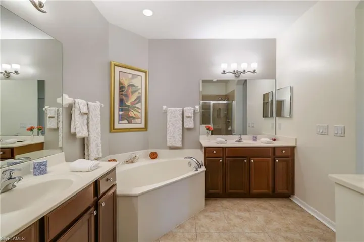 Bathroom featuring a bath, light tile patterned floors, a stall shower, and two vanities