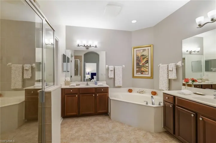 Bathroom featuring a garden tub, a shower stall, light tile patterned flooring, two vanities, and recessed lighting