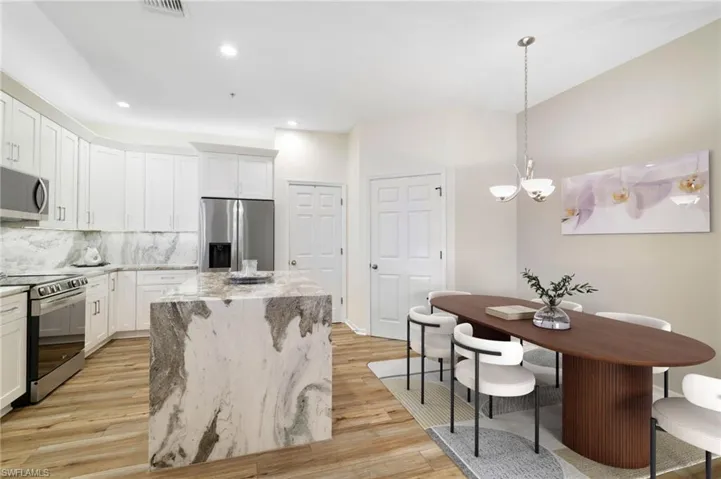 Kitchen with appliances with stainless steel finishes, light stone countertops, white cabinetry, hanging light fixtures, and light wood finished floors