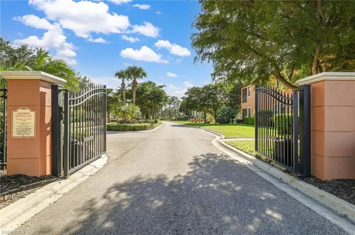 View of asphalt street featuring a gate, curbs, and a gated entry