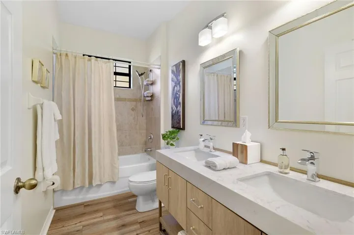 Bathroom with shower / bathtub combination with curtain, light wood finished floors, and double vanity