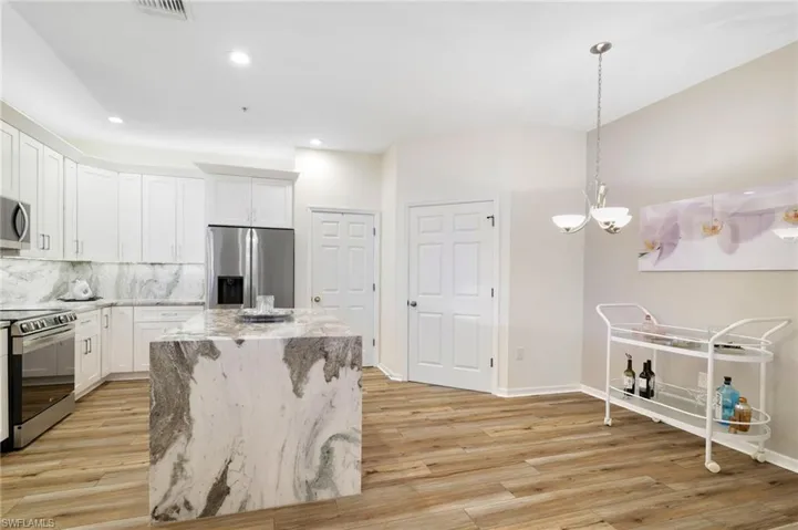 Kitchen featuring appliances with stainless steel finishes, tasteful backsplash, light stone counters, white cabinets, and hanging light fixtures