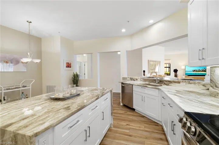 Kitchen featuring white cabinets, stainless steel appliances, light stone countertops, light wood finished floors, and pendant lighting