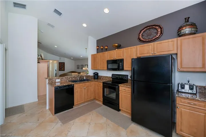 Kitchen with vaulted ceiling, visible vents, a sink, and black appliances