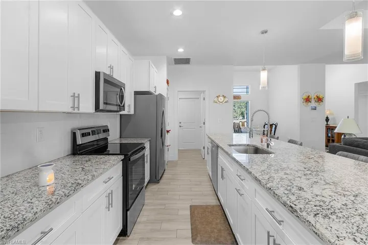 Kitchen with hanging light fixtures, appliances with stainless steel finishes, sink, and white cabinets