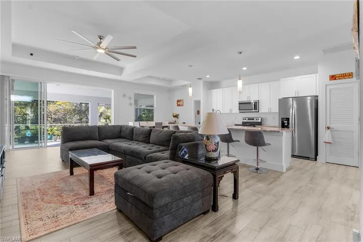 Living room with light hardwood / wood-style floors, ceiling fan, and a tray ceiling