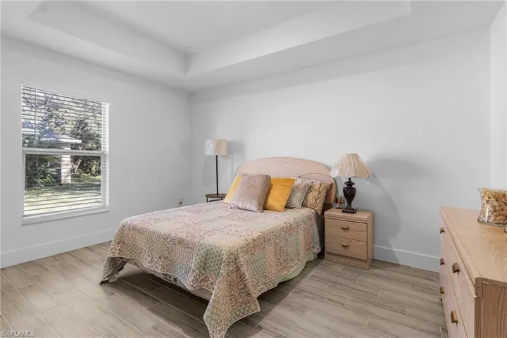 Bedroom featuring a raised ceiling, light wood-type flooring, and multiple windows