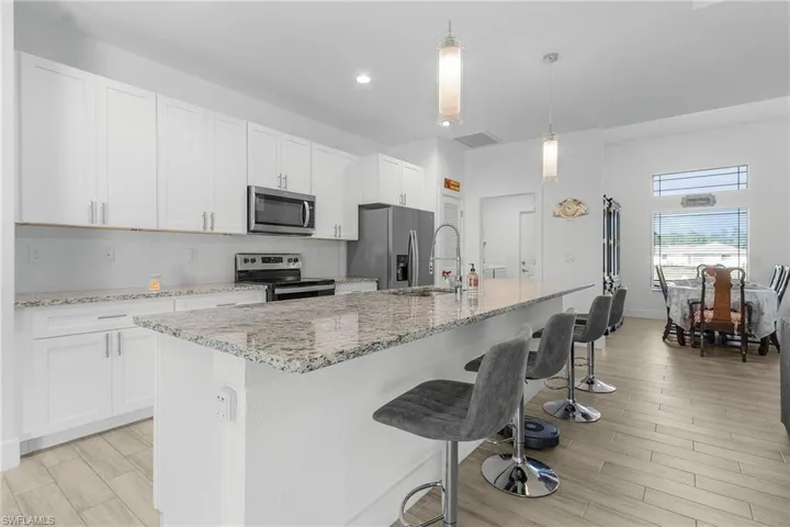 Kitchen featuring stainless steel appliances, pendant lighting, a center island with sink, and white cabinets