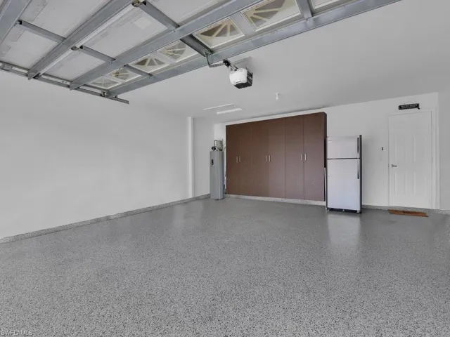 Garage with freestanding refrigerator, a garage door opener, and water heater