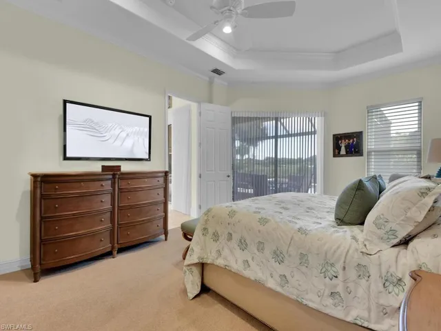 Carpeted bedroom featuring a tray ceiling, crown molding, access to outside, and ceiling fan
