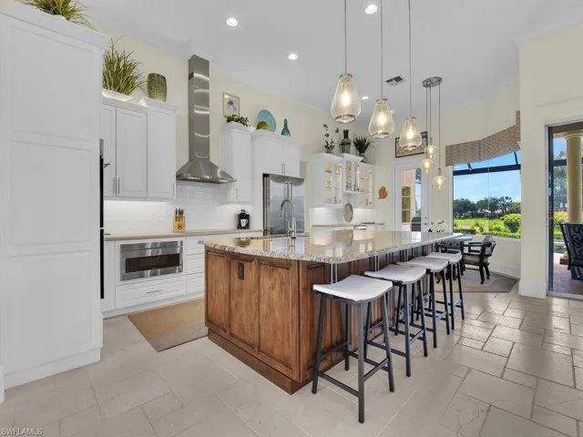 Kitchen with wall chimney range hood, recessed lighting, high quality fridge, tasteful backsplash, and a spacious island
