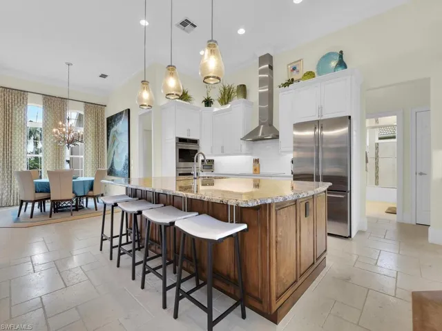 Kitchen with appliances with stainless steel finishes, wall chimney range hood, stone tile flooring, a chandelier, and light stone counters
