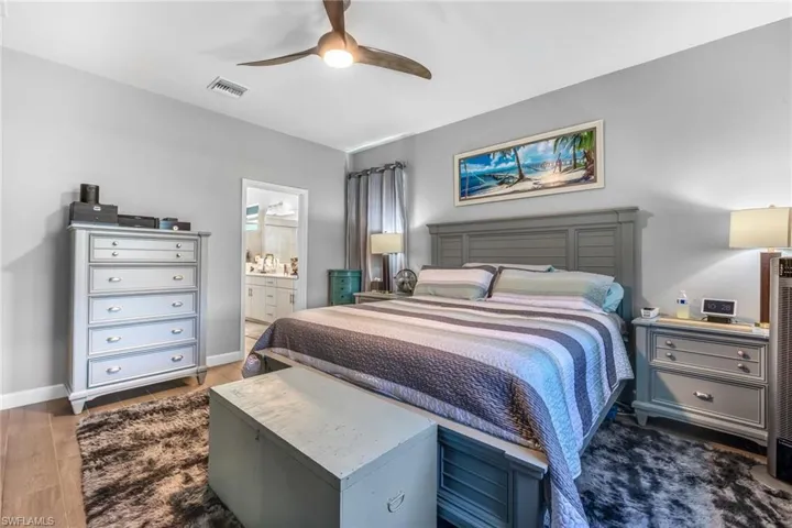 Bedroom with wood finished floors, visible vents, ensuite bath, baseboards, and ceiling fan