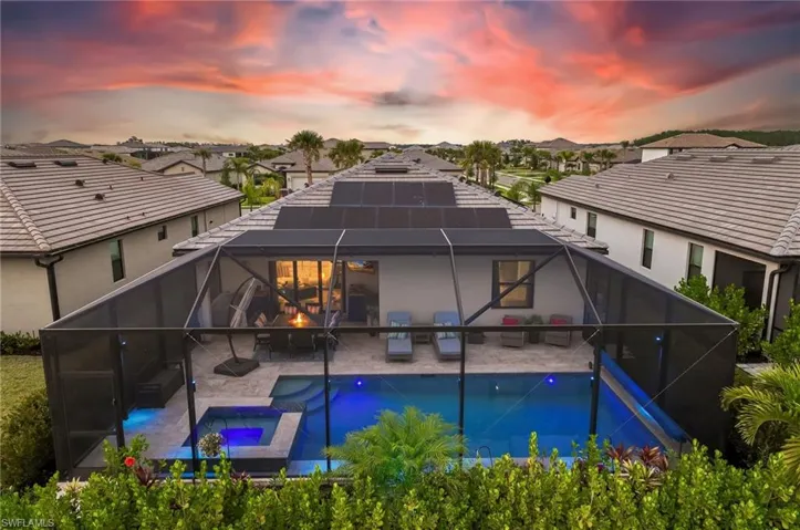 Back of house at dusk with glass enclosure, a residential view, a patio, and a pool with connected hot tub