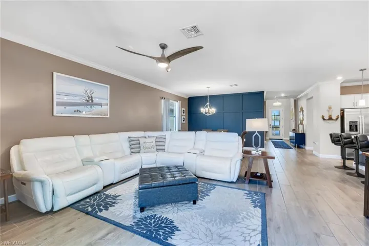 Living room featuring visible vents, light wood finished floors, ornamental molding, and ceiling fan with notable chandelier