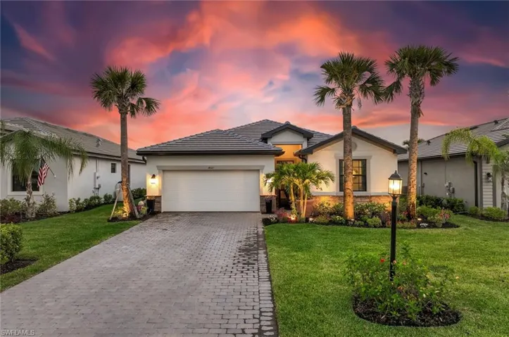 Ranch-style home with an attached garage, a lawn, stucco siding, and decorative driveway