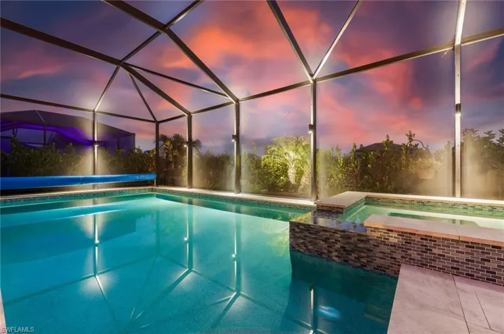 View of swimming pool featuring glass enclosure and a pool with connected hot tub