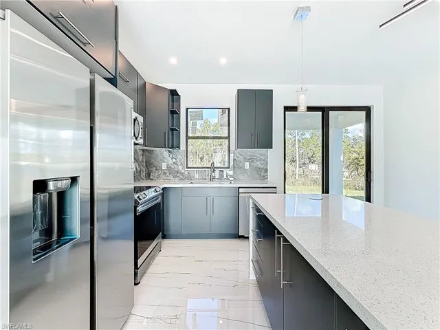 Kitchen with stainless steel appliances, recessed lighting, light marble finish flooring, light stone countertops, and hanging light fixtures