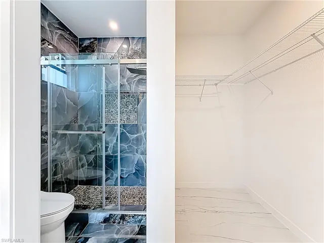 Full bath with marble look tile flooring, a spacious closet, and a marble finish shower