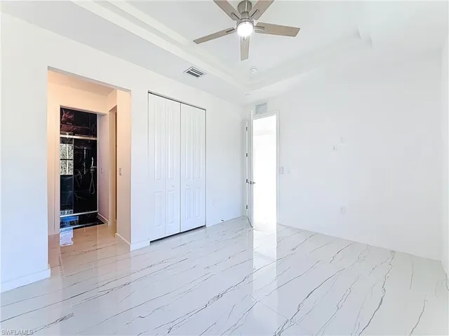 Unfurnished bedroom with a closet, ceiling fan, a raised ceiling, and light marble finish floors