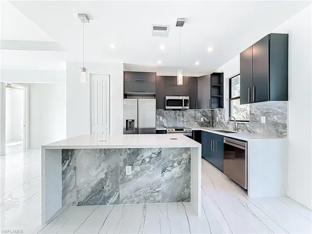 Kitchen with hanging light fixtures, light stone counters, stainless steel appliances, a center island, and modern cabinets
