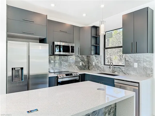 Kitchen featuring appliances with stainless steel finishes, light stone counters, decorative light fixtures, open shelves, and backsplash