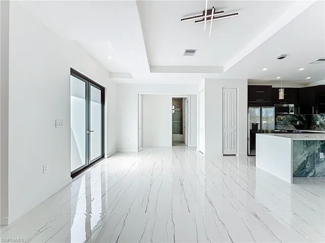 Unfurnished living room with recessed lighting, a tray ceiling, and light marble finish floors