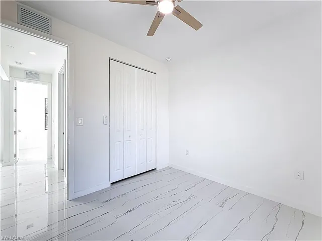 Unfurnished bedroom featuring a closet, light marble finish floors, and ceiling fan